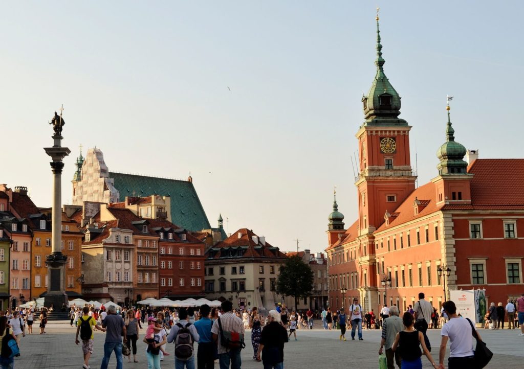 Lively scene in Warsaw's Old Town Square featuring Sigismund's Column and the Royal Castle tower.